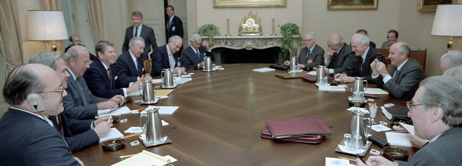 Fifteenwhite guys in ties and jackets sitting around a large oval table, with coffeepots and manila folders.  Reagan and Gorbachev sit on opposite sides, both flanked by advisers.