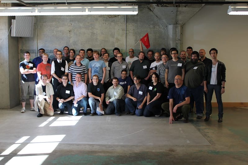 three rows of white guys, with a white woman and a couple of guys who aren't white mixed in, mostly in t-shirts or polo shirts.