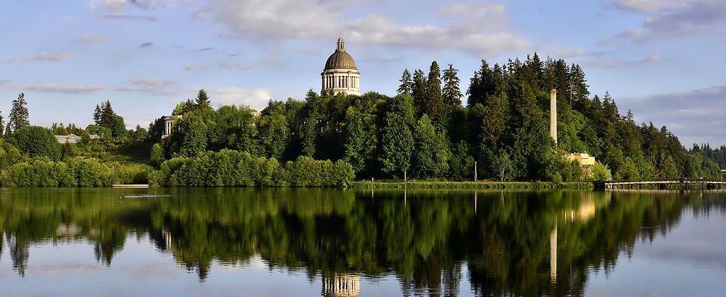 The dome of a bulding above a row of trees, with reflections in a lake